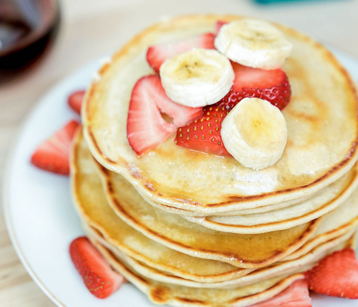 stack of buttermilk pancakes with strawberries and bananas on top